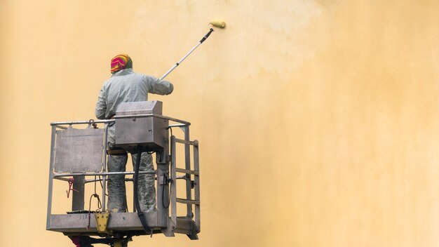 man-lifting-platform-painting-building-wall-with-roller-exterior-outdoors_358642-21